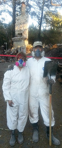 Bill and Vicky standing in protective clothing in front of the the remains of their home