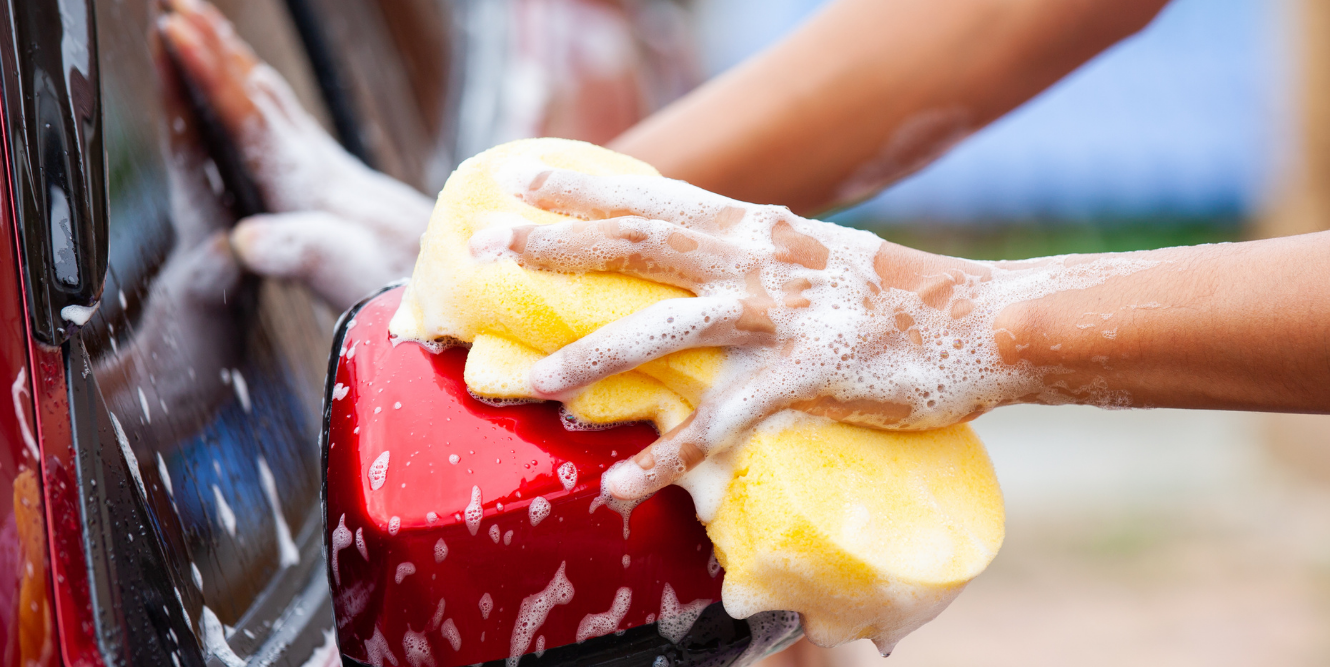 Image of a hand with a soapy sponge about to wash a red car